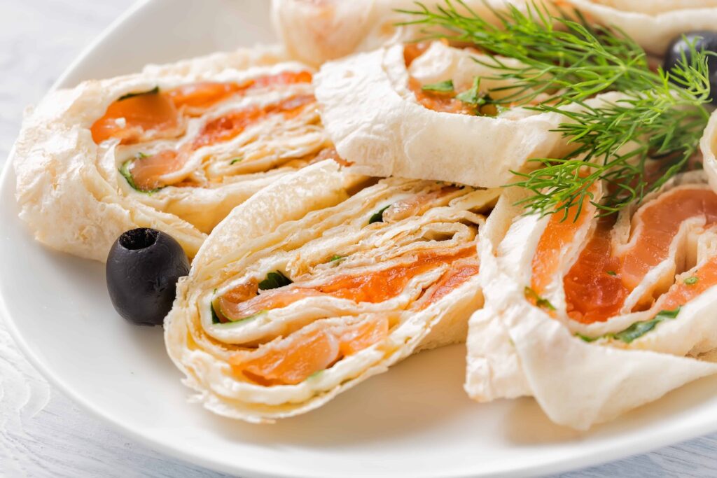 rotoli-di-lavash-di-salmone-con-aneto-formaggio-e-olive-nere-sul-piatto-bianco-1
